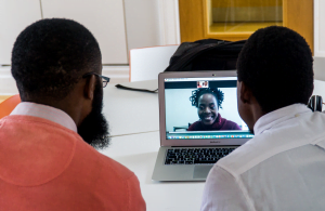 Two men look at a computer where a woman is on a video call