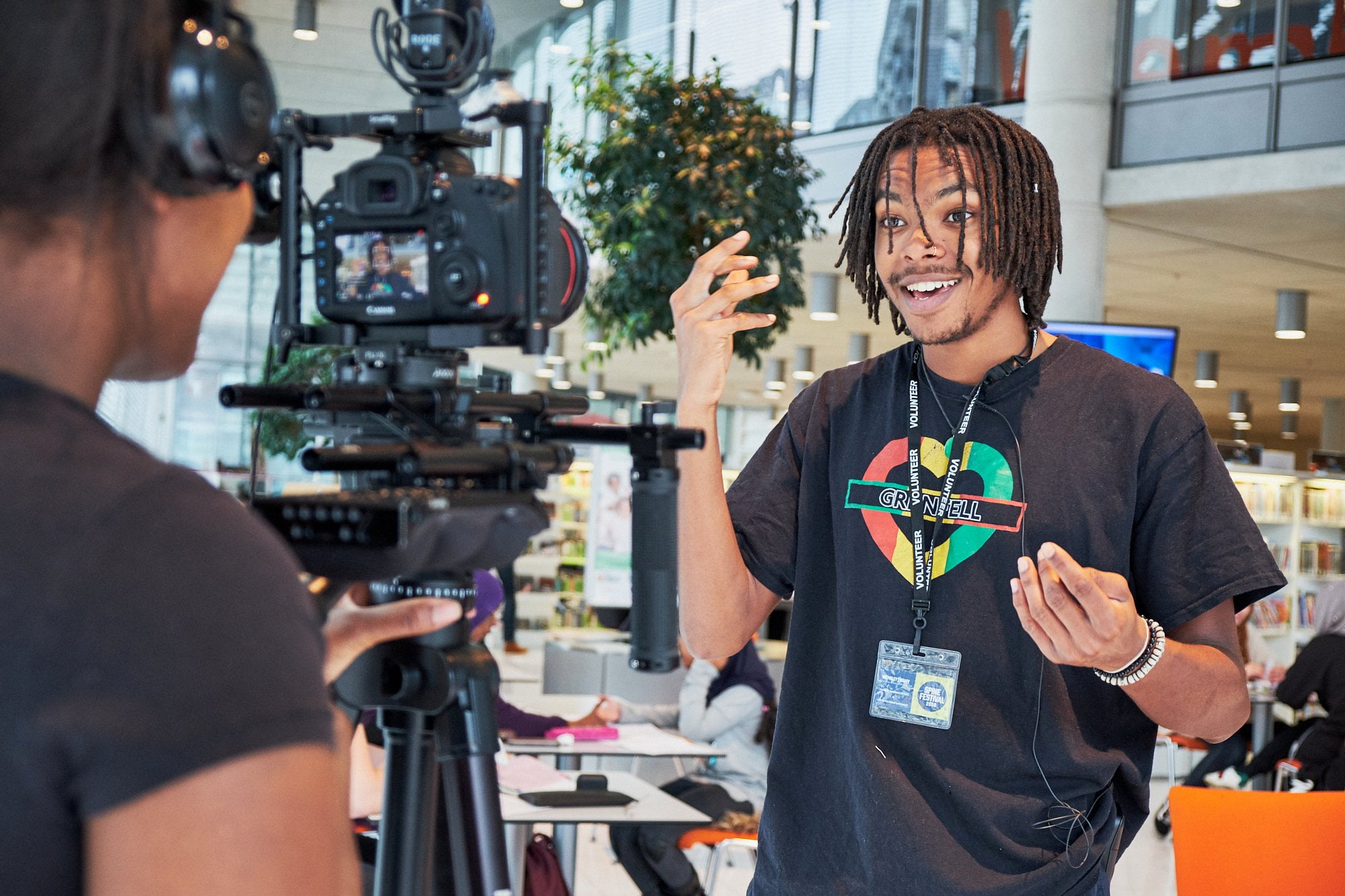Young man with locks smiles and gesticulates while being filmed