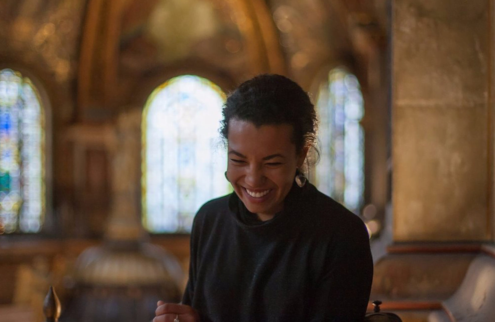 A smiling woman in a church wearing dark clothes. She's happy.