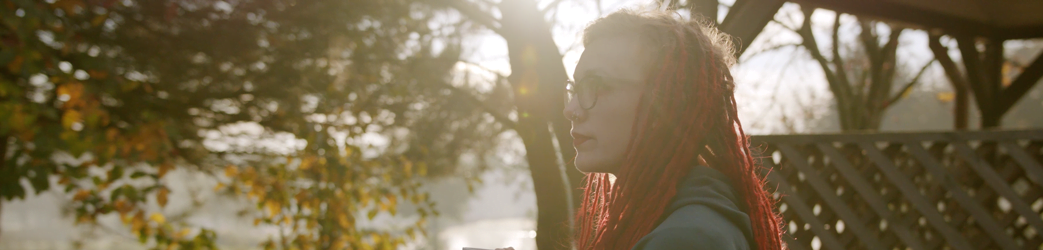 A young lady with braided red hair against a backdrop of sunshine coming through the trees