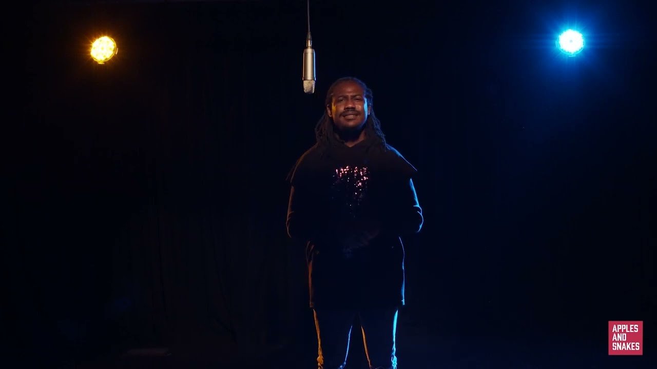 Screenshot from a video of Chika speaking into a microphone in a dark room with blue and yellow lights