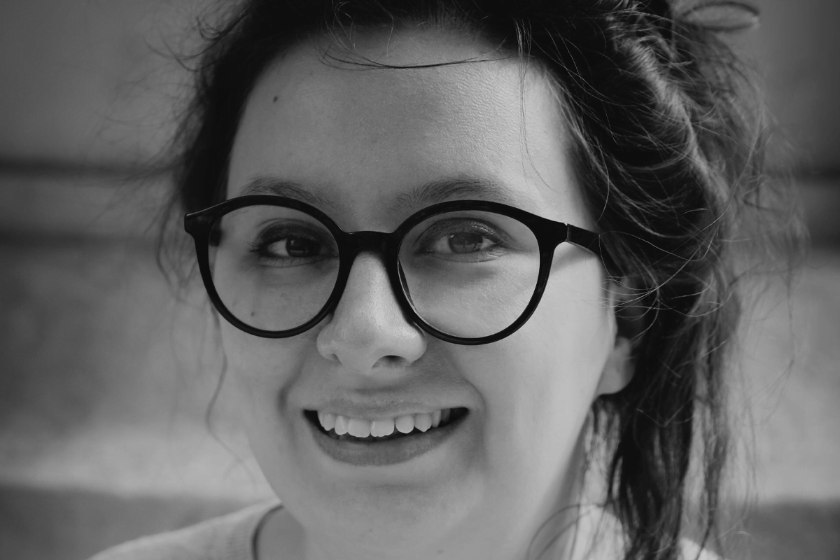 A woman with dark rimmed glasses and loosely tied up hair, with an open smile