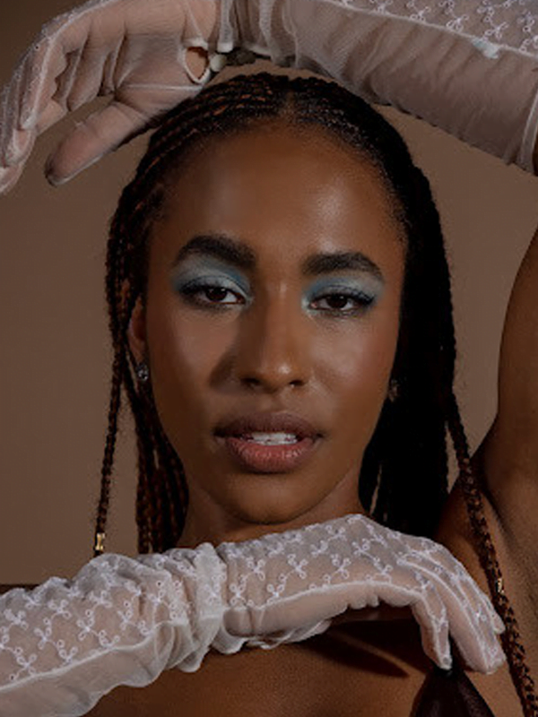Binta wears white lace gloves with one arm above and one below face. Frosted blue eye shadow and long braided hair