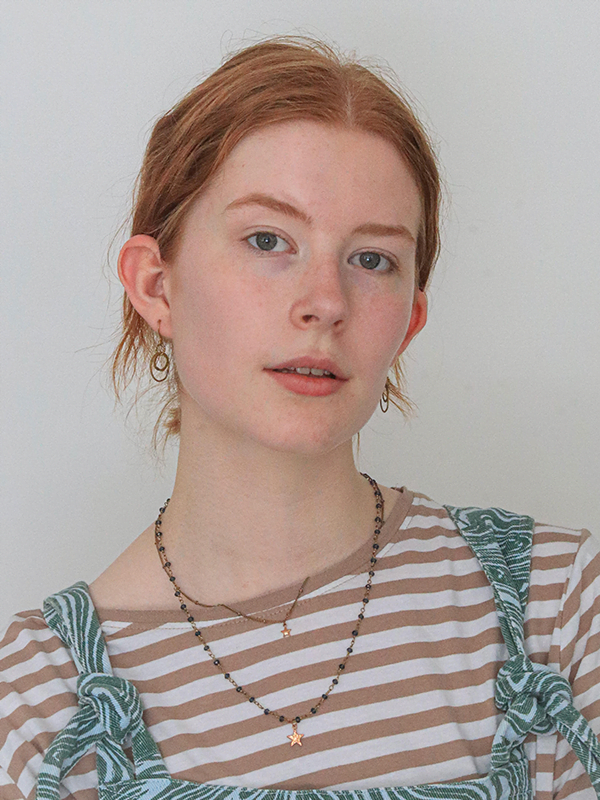 Elena wears ginger hair pulled back, pink and yellow striped top and light denim dunagrees